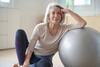 an older woman in yoga clothes leaning against a body ball while sitting on the floor